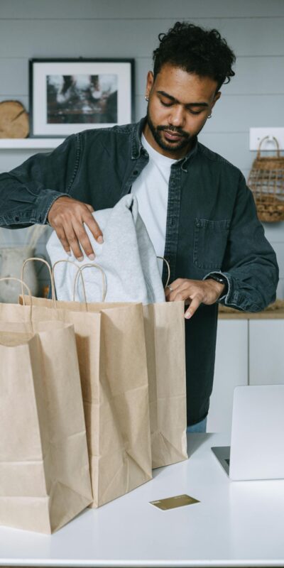 Adult man organizing purchases with paper bags and laptop in a modern home setting.